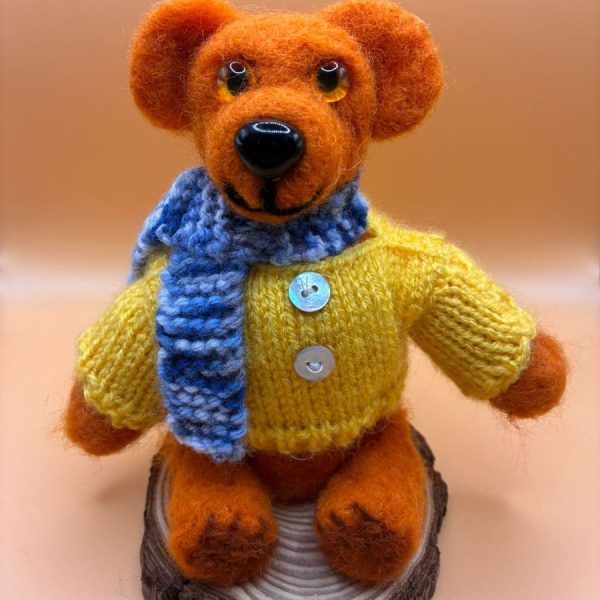 Bear in yellow jumper and blue scarf on wood slice